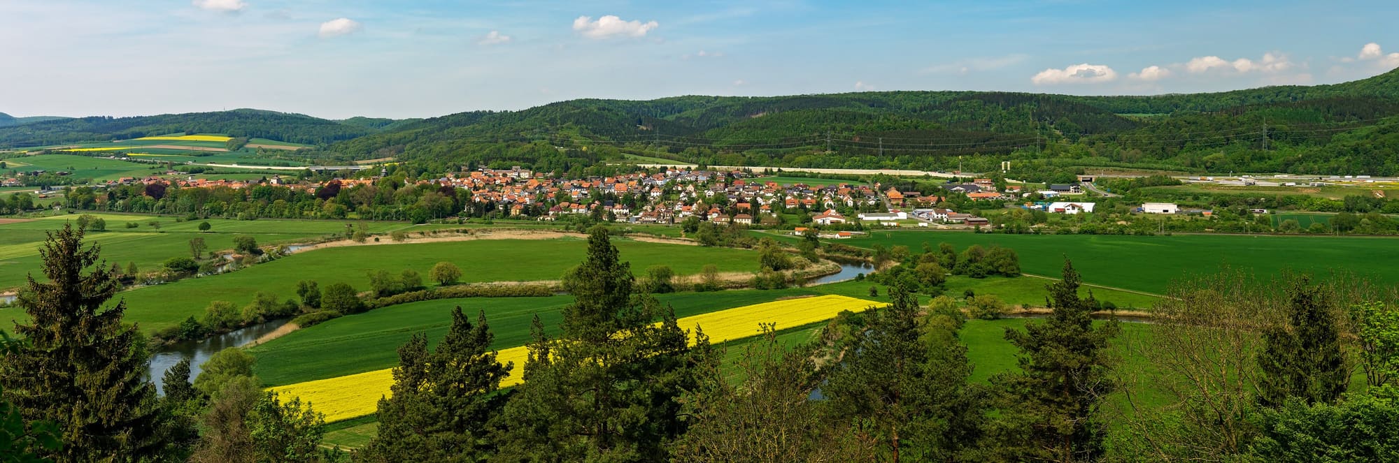 Landschaft mit Dorf, Feldern, Raps und bewaldeten Hügeln