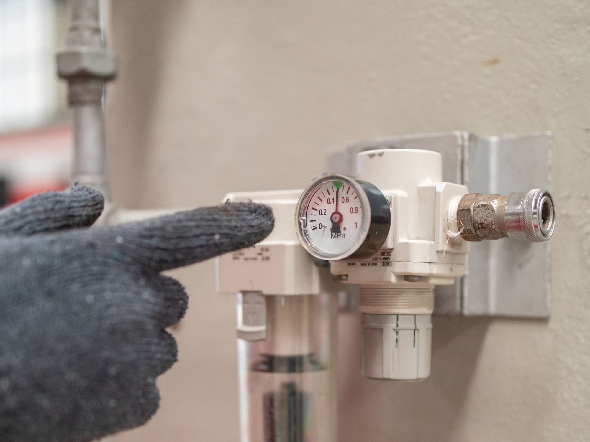 Hand im Arbeitshandschuh zeigt auf das Manometer einer Druckluft-Wartungseinheit